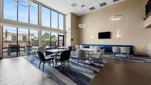 A modern hotel lobby with large windows, a flat-screen TV, and a mix of seating areas including tables and sofas. - Comfort Inn Aikens Center (Martinsburg)