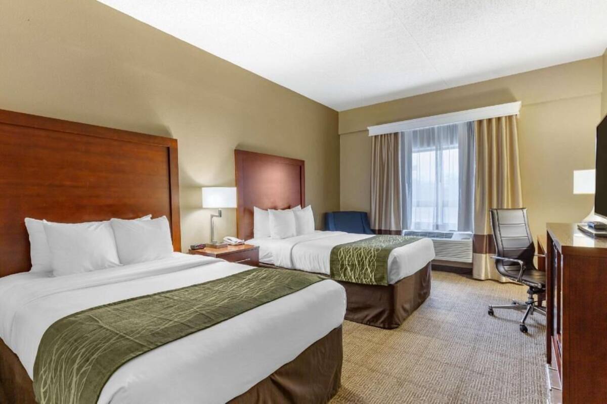 A hotel room with two beds, a desk, a chair, and a large window with curtains.