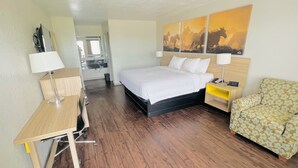 A hotel room with a bed, bedside tables, a desk, a chair, and artwork on the wall.