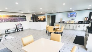 A modern dining area with a large table and chairs, a kitchen area with white cabinets, and a TV mounted on the wall.