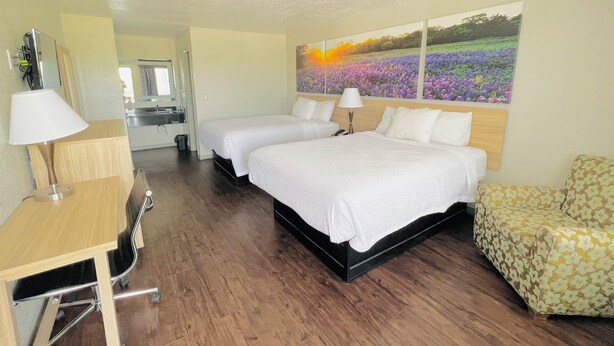 A hotel room with two beds, a desk, a chair, and a large floral painting on the wall.