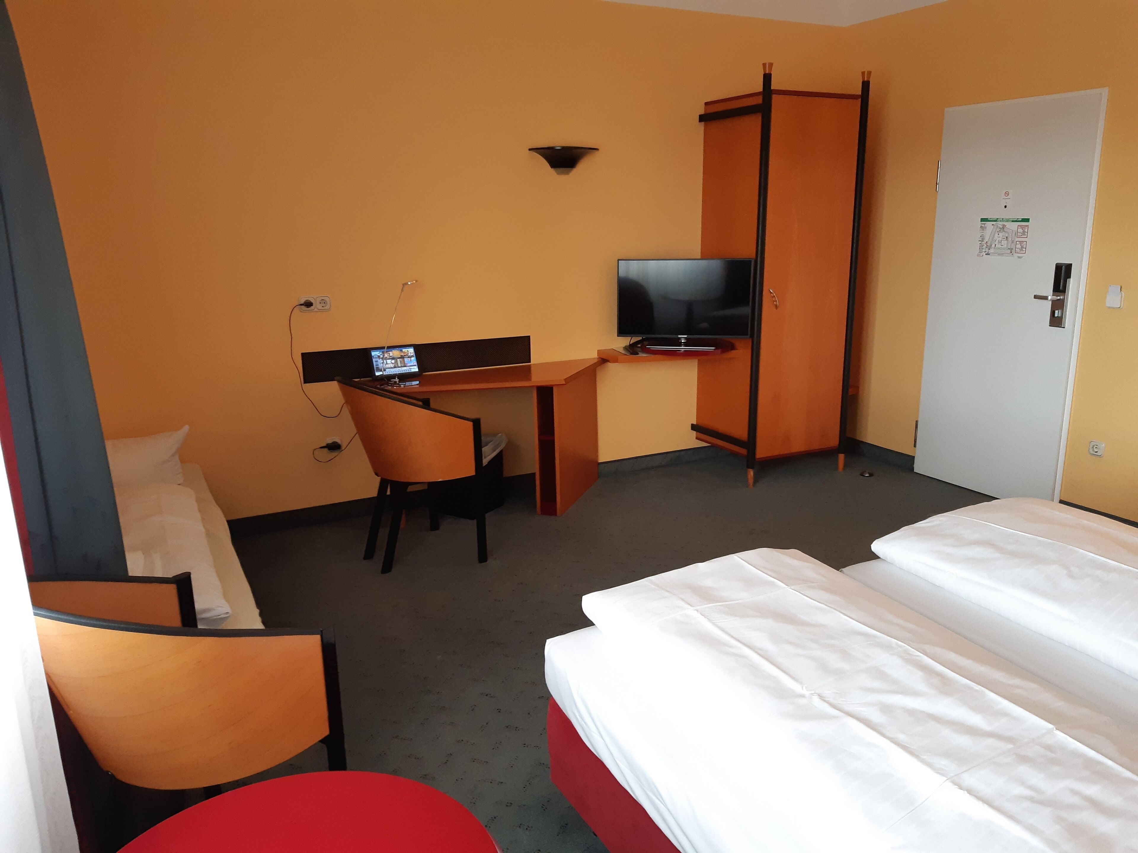 Una habitación de hotel con una cama, un escritorio con una computadora, un televisor y un armario.