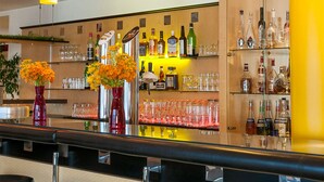 A bar area with shelves of liquor bottles and glasses, a mirror reflecting the bar, and a yellow accent wall.