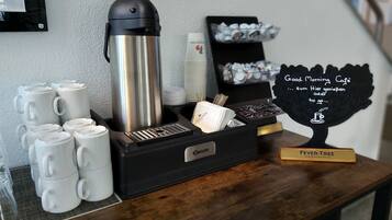 A coffee station with a coffee maker, mugs, and a sign that reads "Good Morning Cafe".