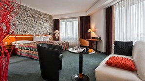 A hotel room with a bed, a sofa, a chair, a small table, and a lamp.