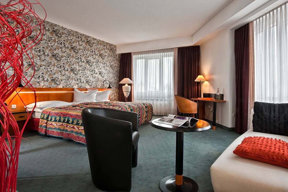 Ein Hotelzimmer mit Bett, einer Couch, einem Sessel, einem kleinen Tisch und einer Lampe.