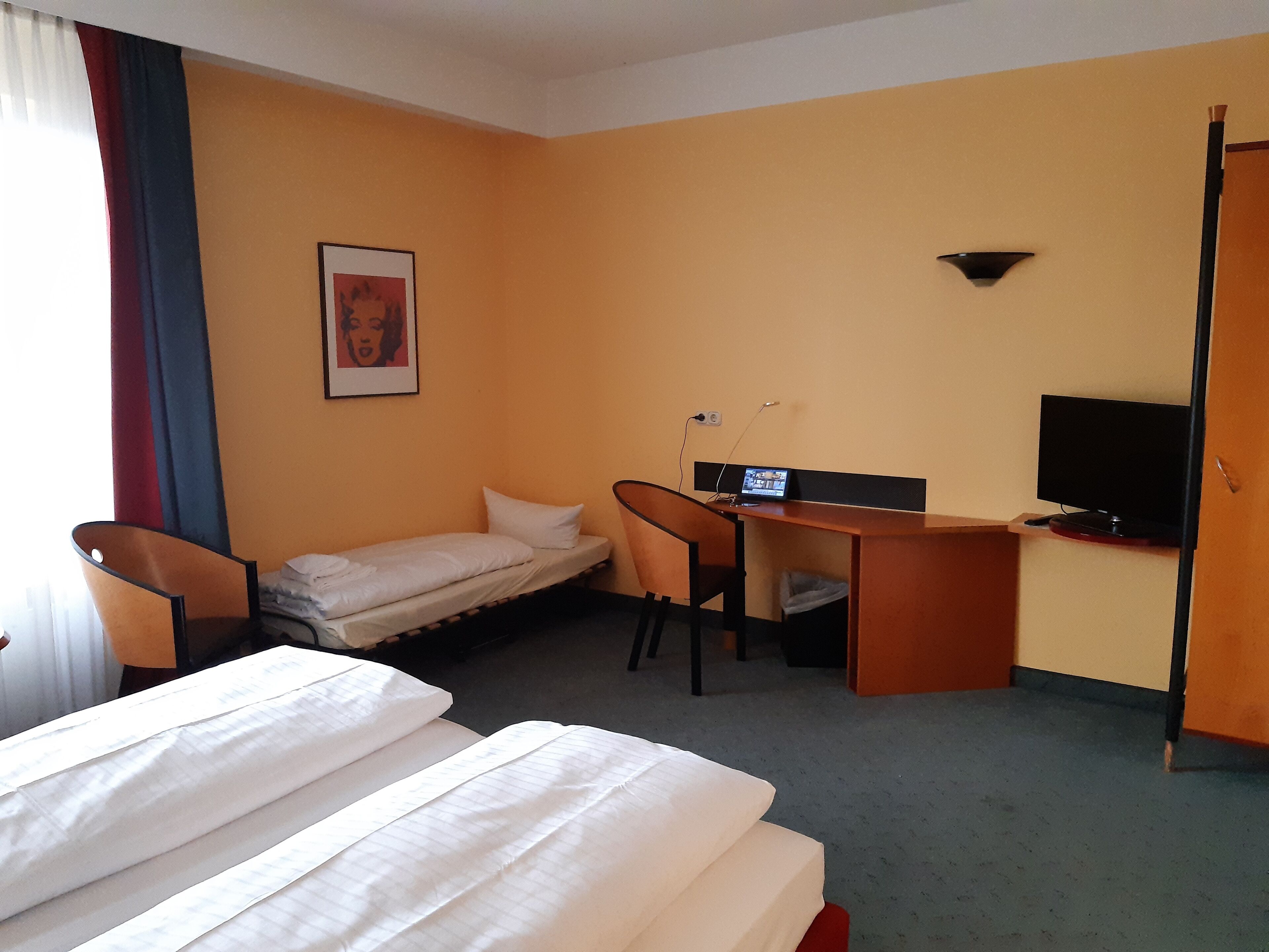 Una habitación de hotel con una cama, un escritorio con computadora, televisor y una silla.