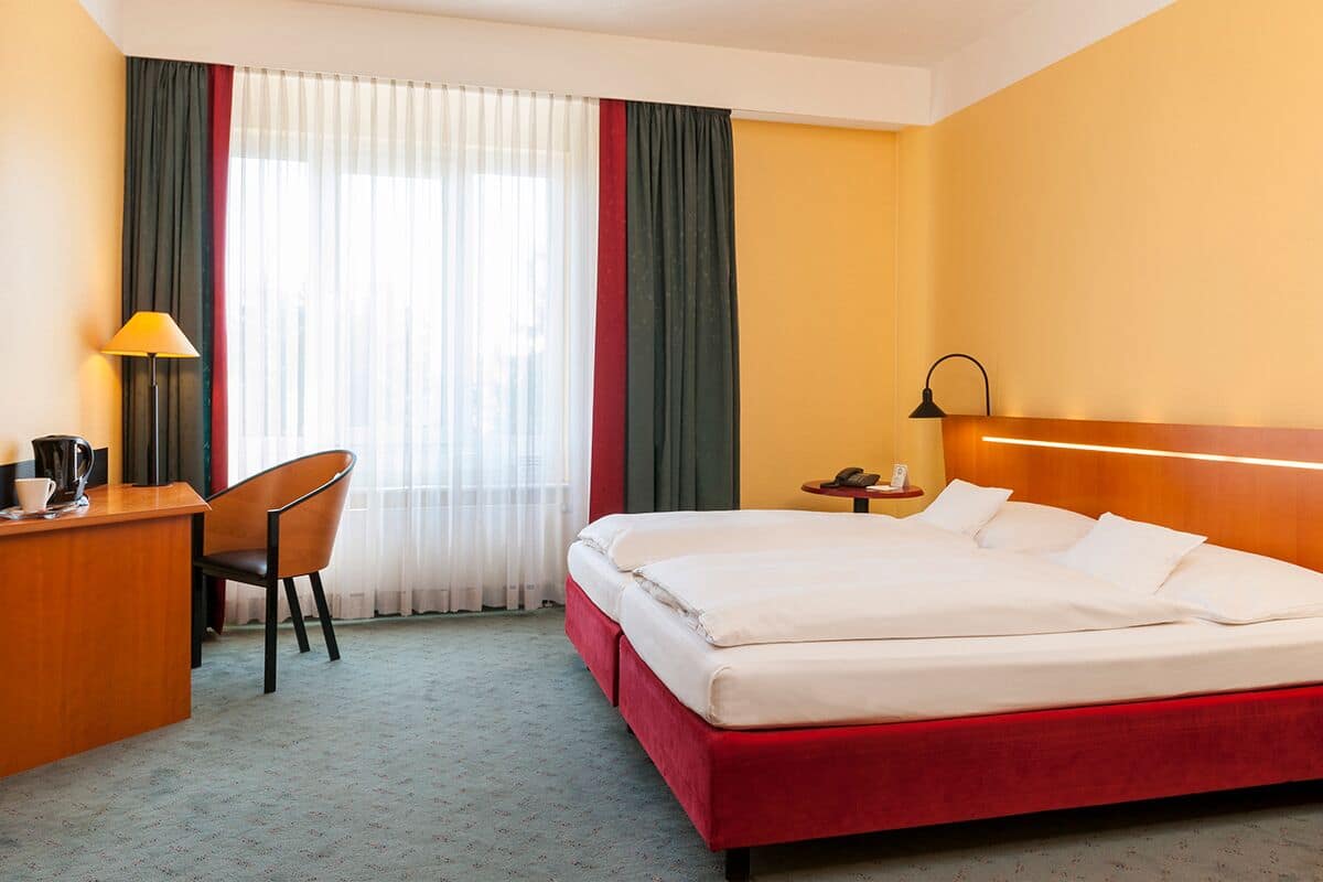 Ein Hotelzimmer mit Bett, Schreibtisch, Stuhl, Lampe und Nachttisch.
