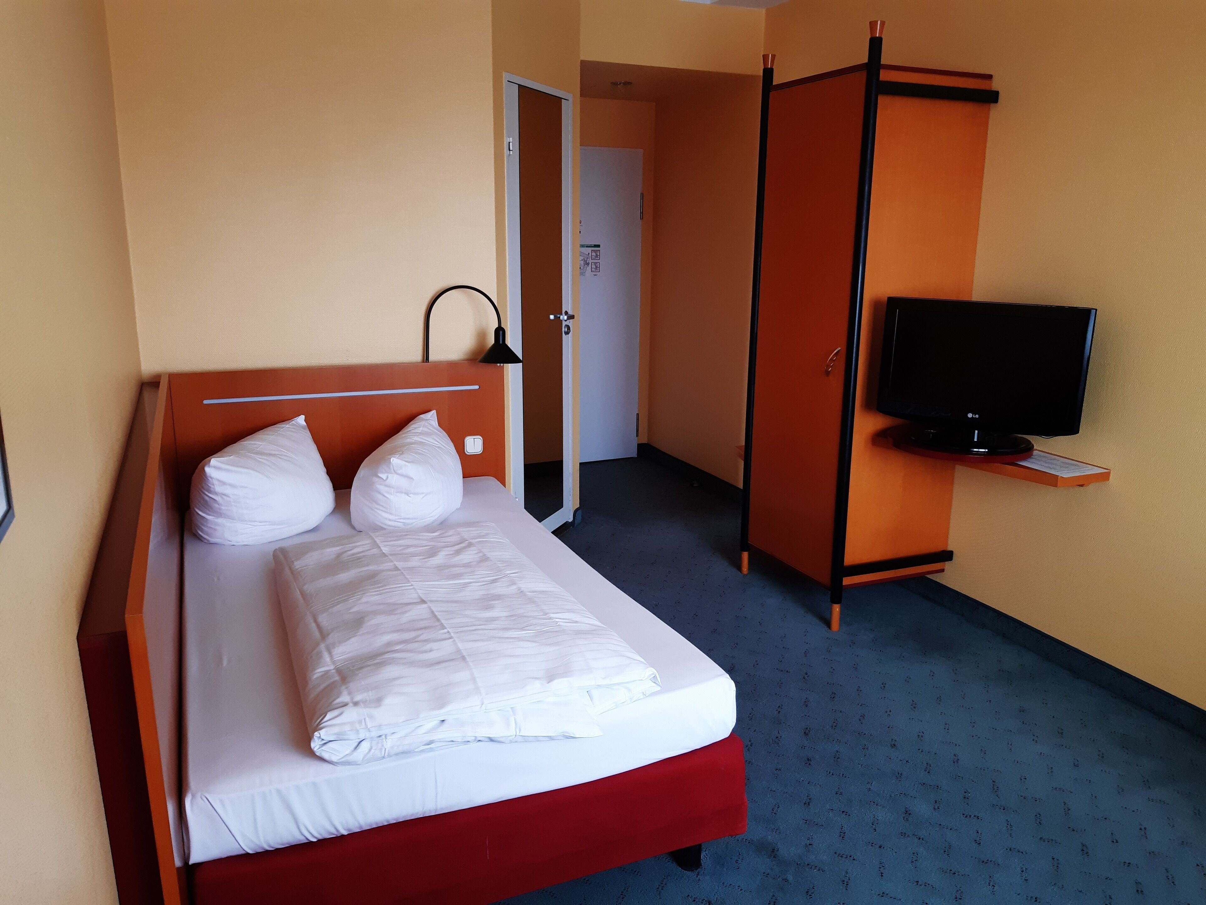 Una habitación de hotel con una cama, televisión y armario.
