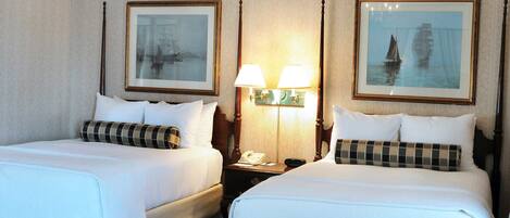 A hotel room with two beds, a nightstand with a lamp, and framed artwork on the walls.