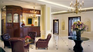 A lobby with a reception desk, leather armchairs, a glass coffee table, a chandelier, and a floral arrangement.