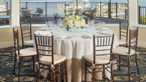 A dining area with a table set for six, a chandelier, and a view of the water and boats.