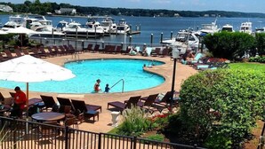 A pool area with lounge chairs and umbrellas, surrounded by a fence and a view of boats on the water.
