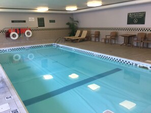 An indoor swimming pool with no diving signs, lifebuoys, and pool rules posted on the wall.