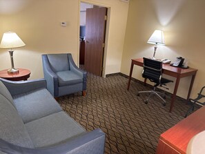 A hotel room with a sofa, a chair, a desk, and a lamp.