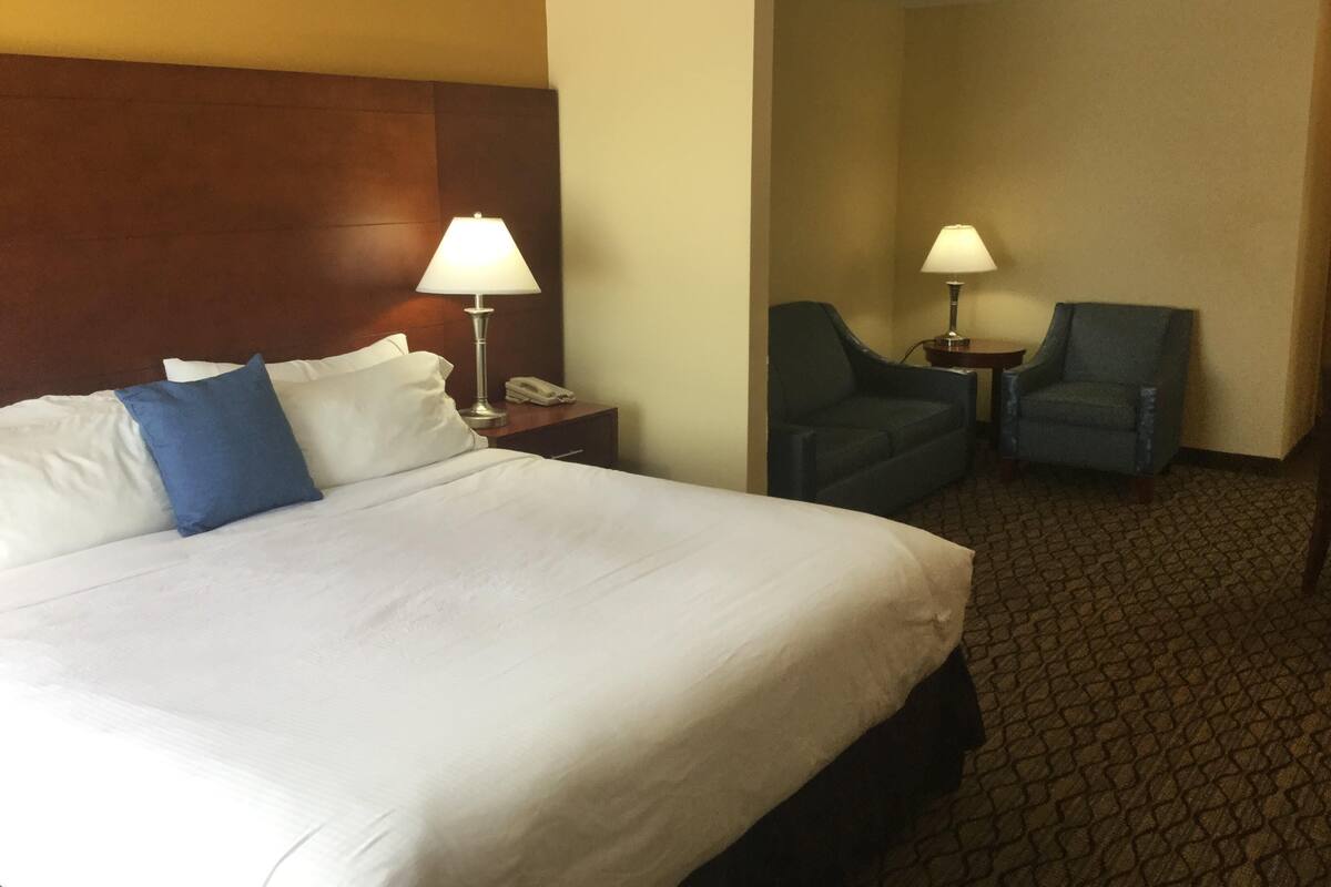 Une chambre d’hôtel avec un grand lit, deux chaises, une table de chevet avec une lampe et un téléphone.