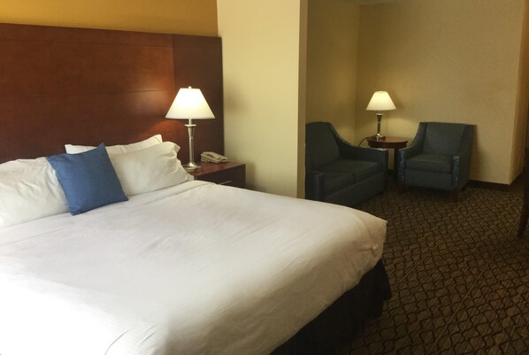 A hotel room with a large bed, two chairs, a nightstand with a lamp, and a telephone.
