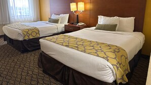A hotel room with two beds, a wooden headboard, a nightstand with a lamp, and a window with curtains.