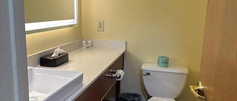 A bathroom with a white sink, mirror, and toilet. There is a trash can and a towel rack.