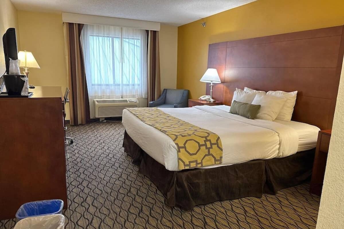 Une chambre d’hôtel avec un grand lit, un bureau avec une lampe, une chaise et une fenêtre avec des rideaux.
