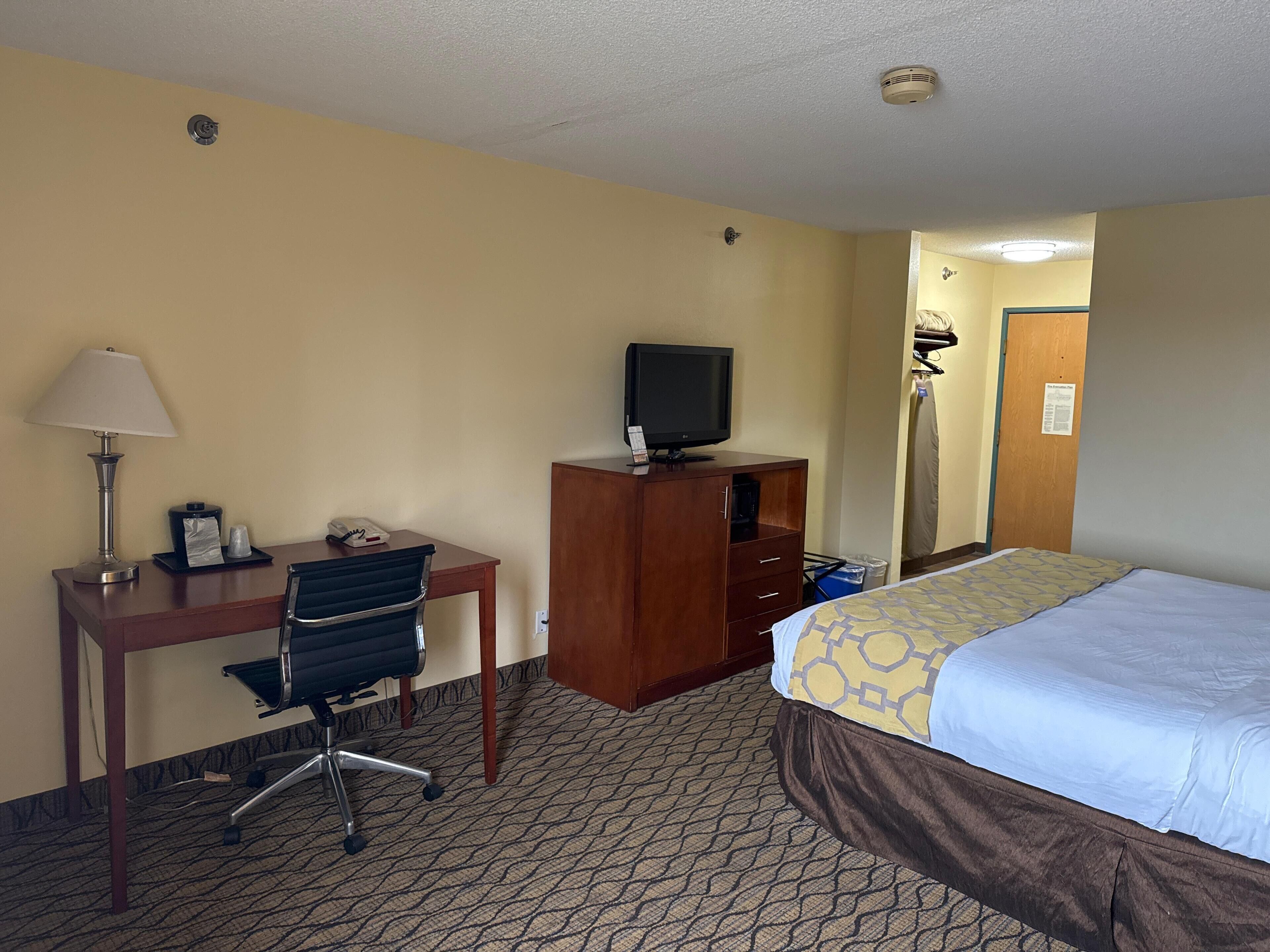 A hotel room with a bed, desk, chair, television, lamp, and a small closet.
