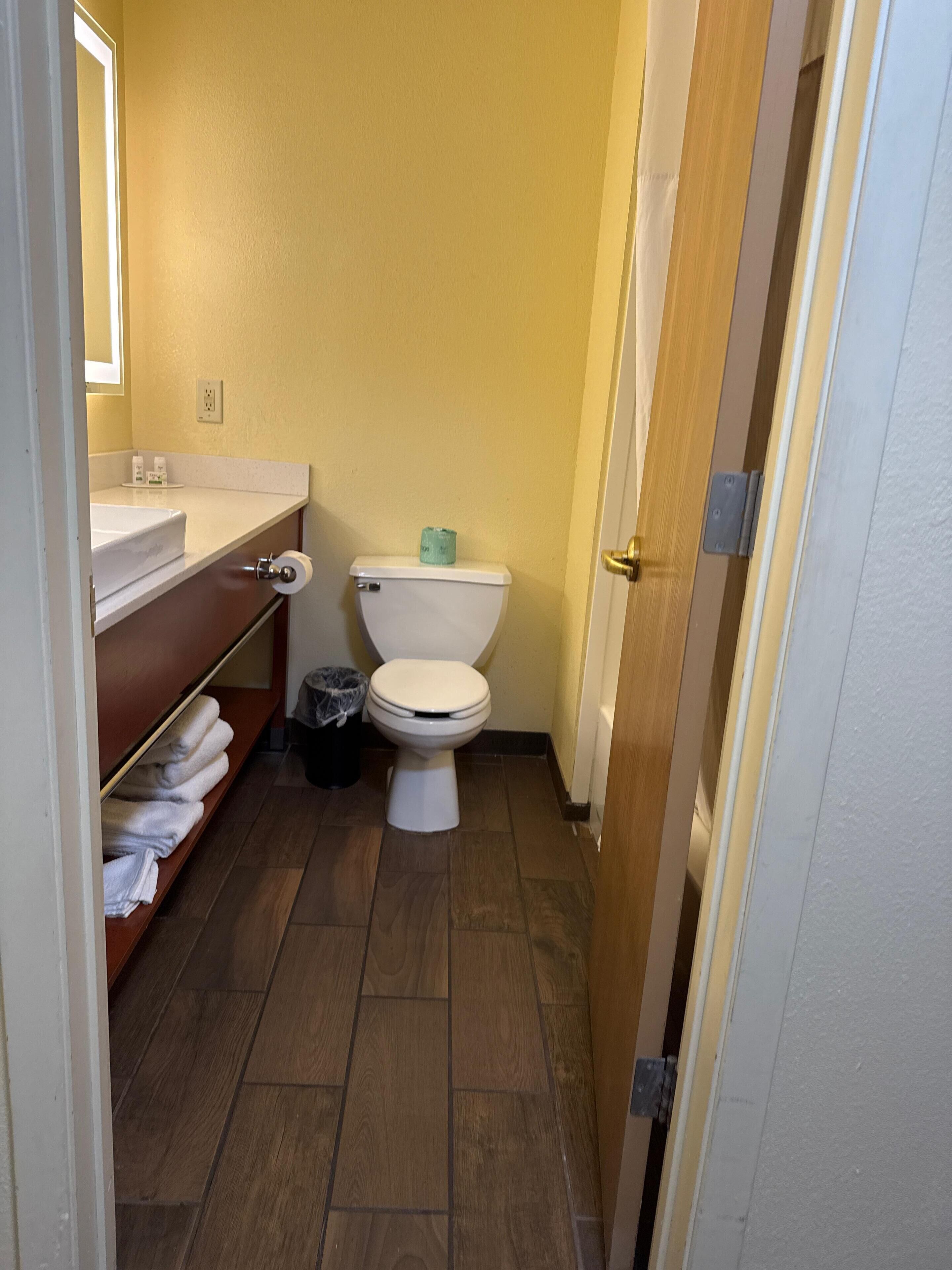 A small bathroom with a toilet, sink, and shelf with towels.