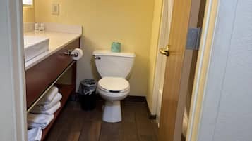 A small bathroom with a toilet, sink, and shelf with towels.
