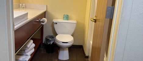 A small bathroom with a toilet, sink, and shelf with towels.