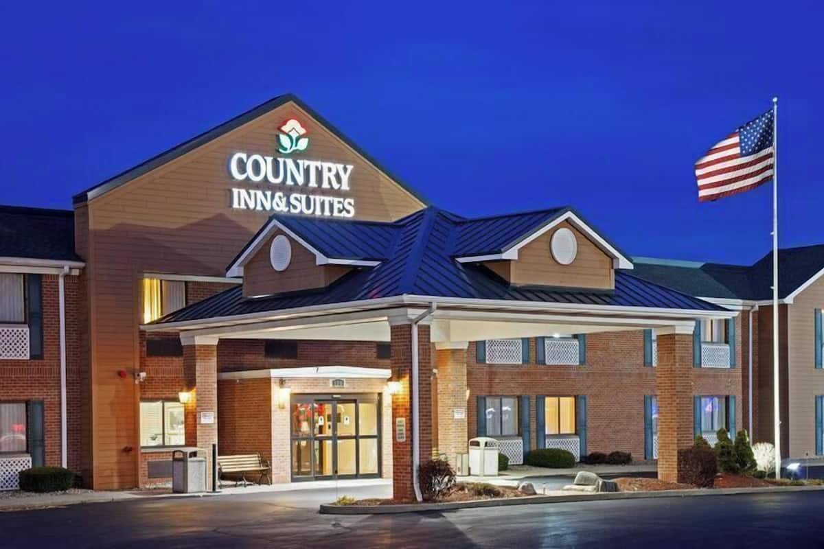 Un bâtiment Country Inn & Suites avec une façade en briques, une entrée couverte et un drapeau américain.
