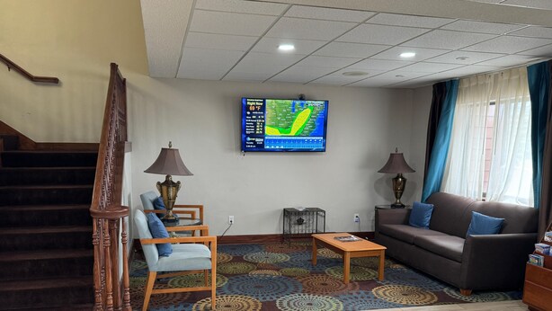 A living room with a staircase, a TV displaying a weather forecast, a sofa, and a patterned rug.