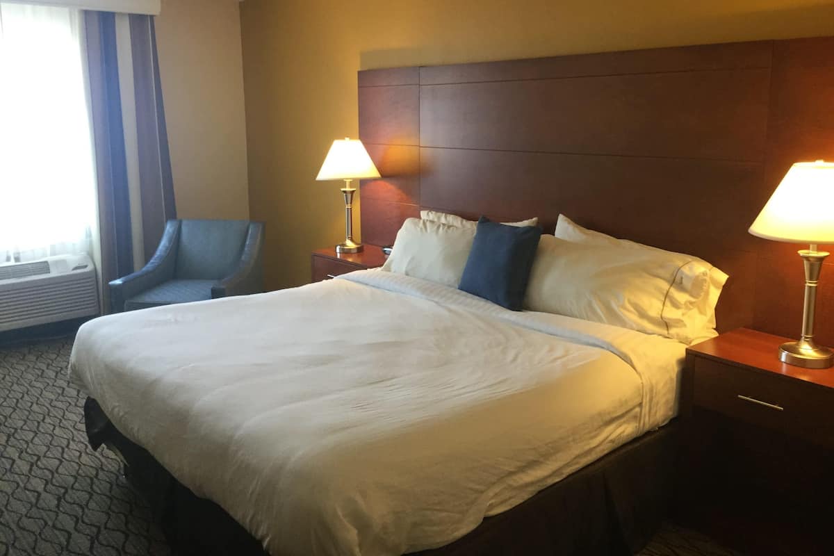 Une chambre d’hôtel avec un grand lit, deux lampes de chevet, une chaise et une fenêtre avec des rideaux.