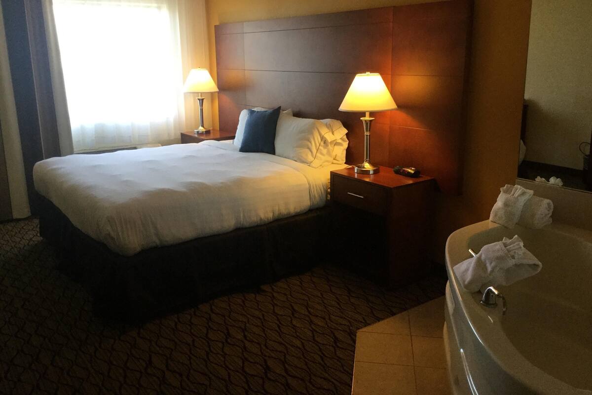 Une chambre d’hôtel avec un grand lit, deux lampes de chevet, une table de chevet, une salle de bain avec une baignoire et un miroir.