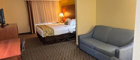 A hotel room with a bed, a sofa, a desk, and a lamp.