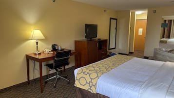 Hotelkamer met bed, bureau, stoel, lamp, televisie en een badkamer met wastafel en spiegel.