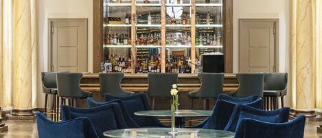 A bar area with a round table and blue chairs, a large liquor display, and a classic ceiling design.
