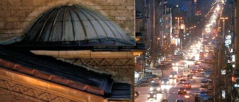 A historic building with arched windows and domed roofs, overlooking a busy street with cars and illuminated signs.