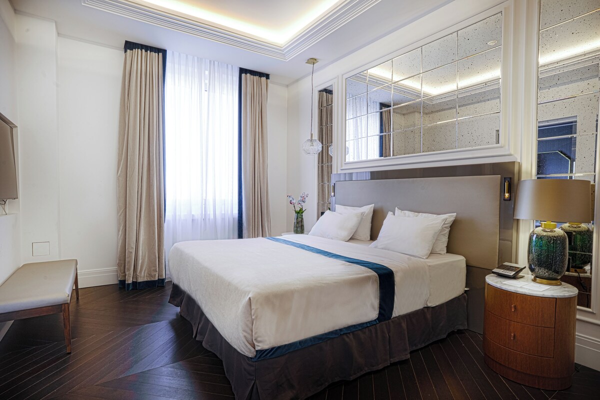 A hotel room with a bed, bedside table, a mirror, and a nightstand.