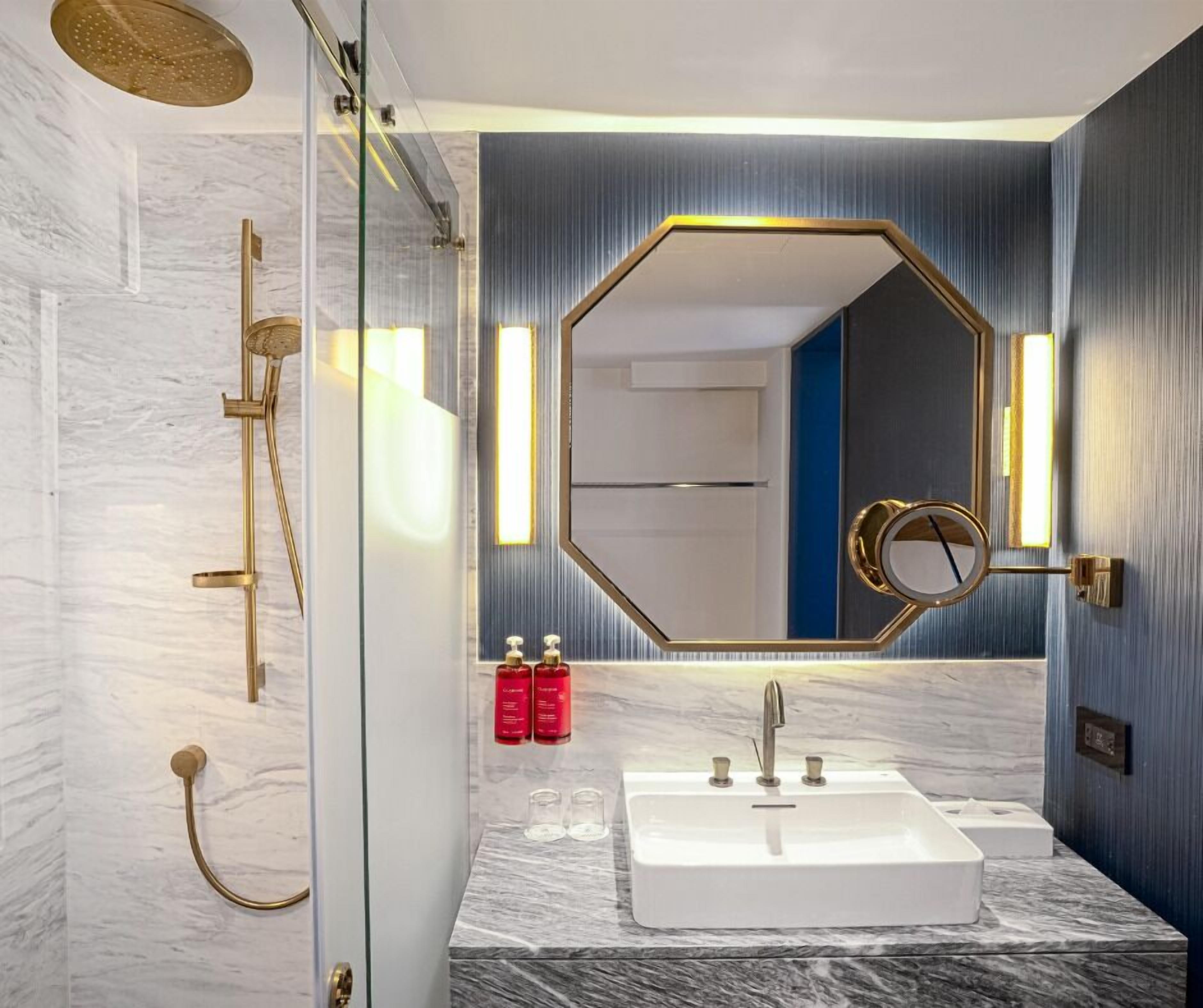 A modern bathroom with a glass-enclosed shower, a white sink, and a large mirror with a gold frame.