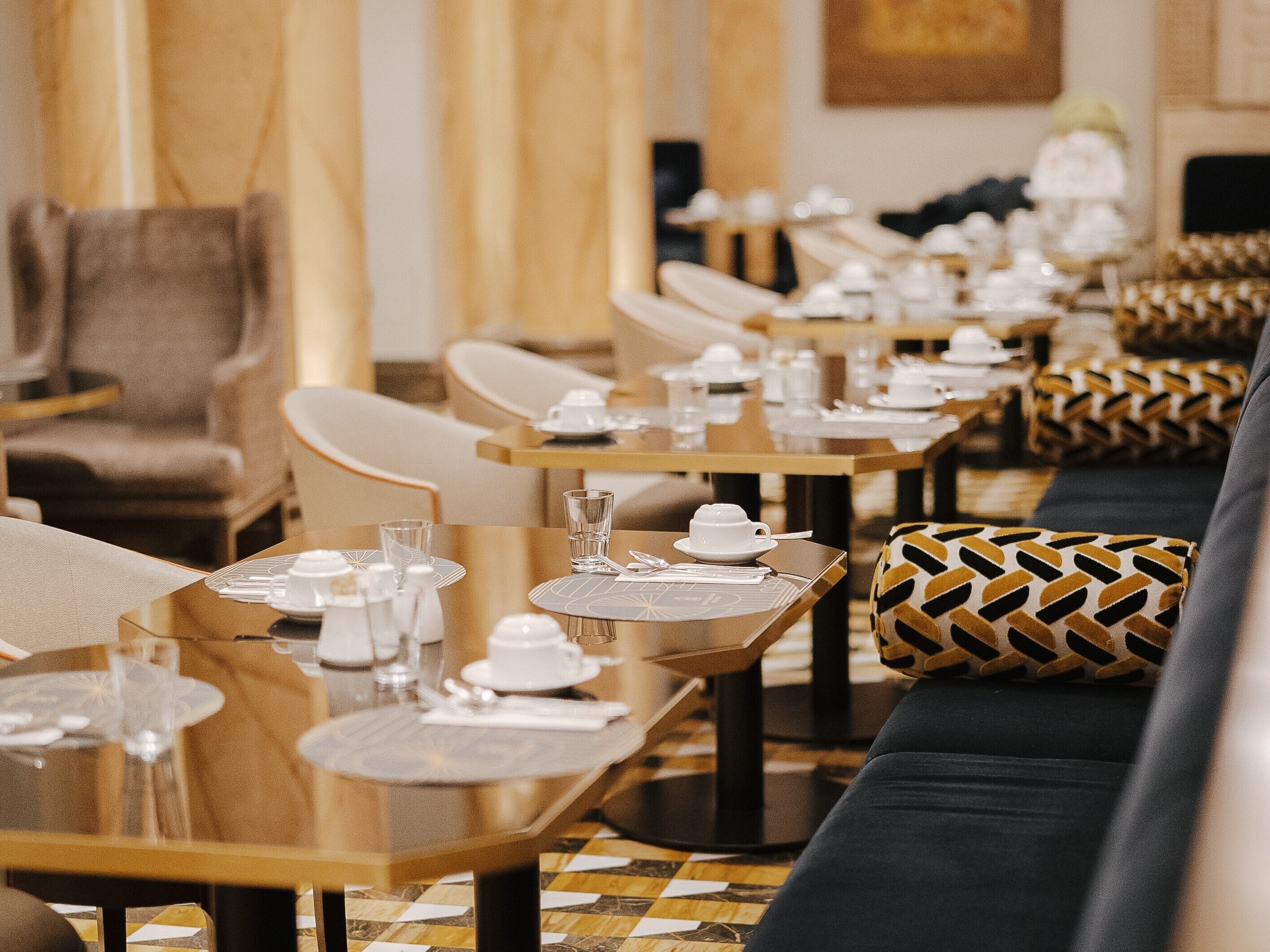 Un restaurante con mesas largas dispuestas para comer, asientos acolchados y un suelo estampado.