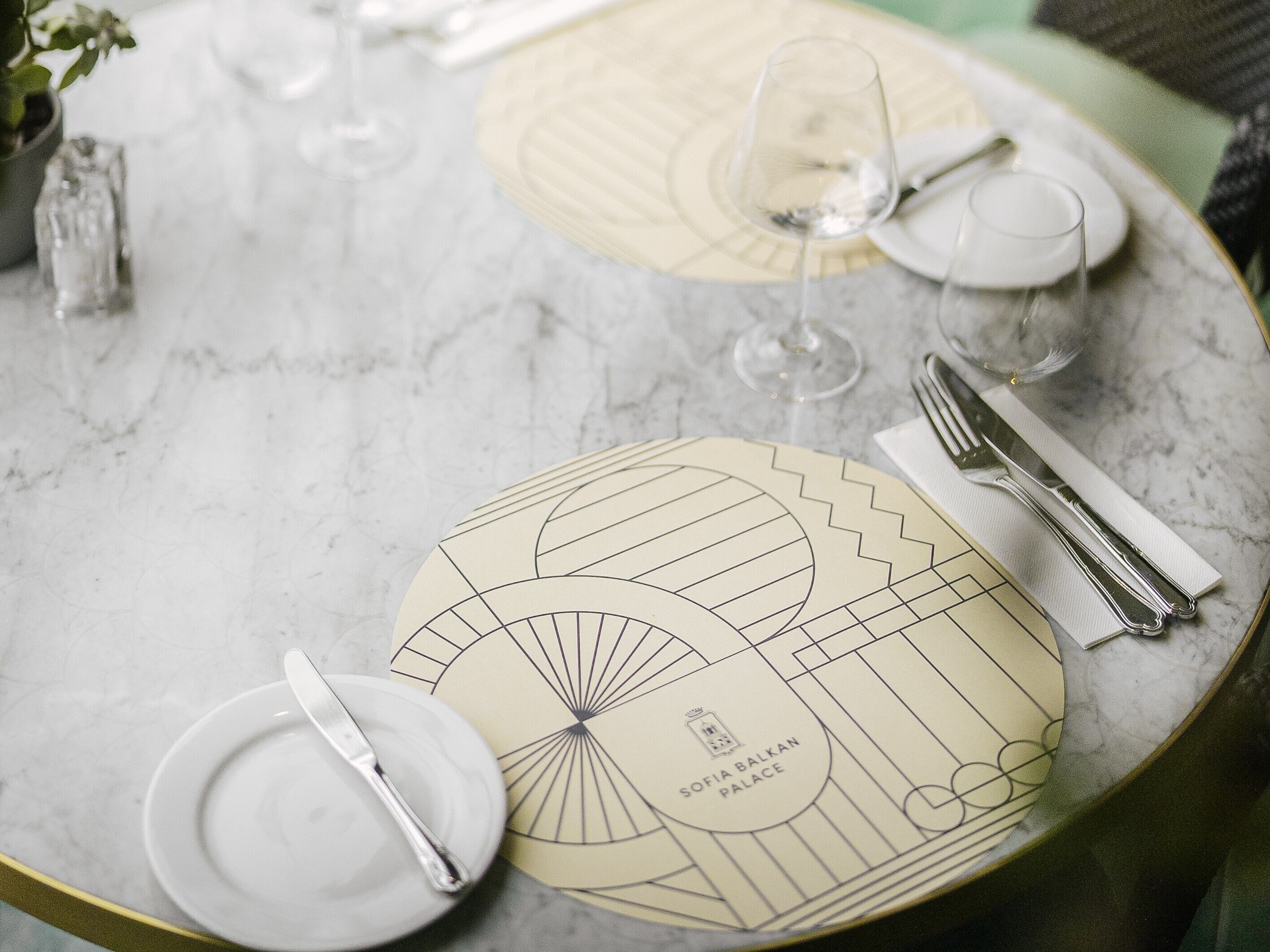 A table set with plates, cutlery, and wine glasses on a marble surface with geometric placemats.