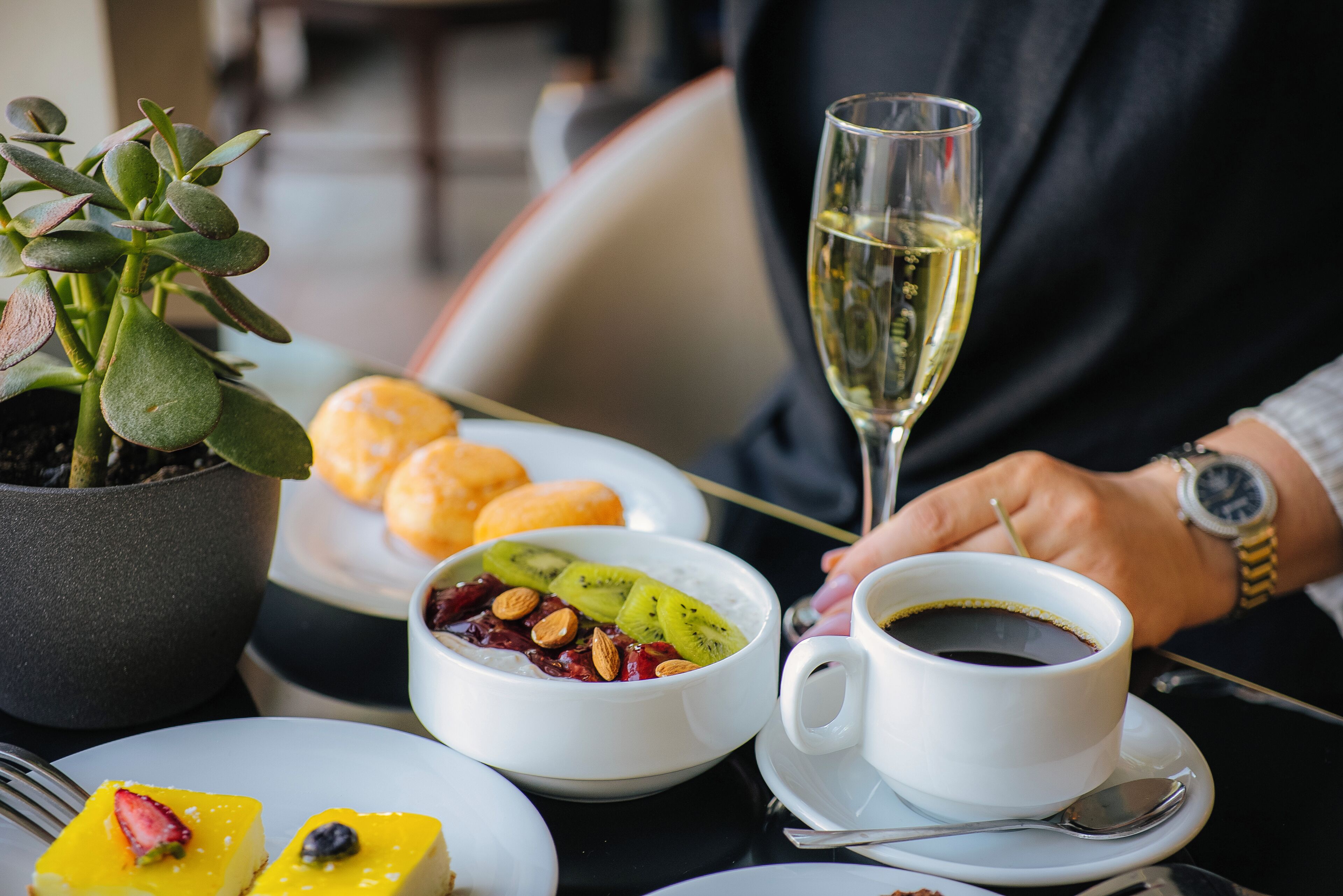 Una mesa con un plato de postre, un bol de fruta, una taza de café y una copa de champán.