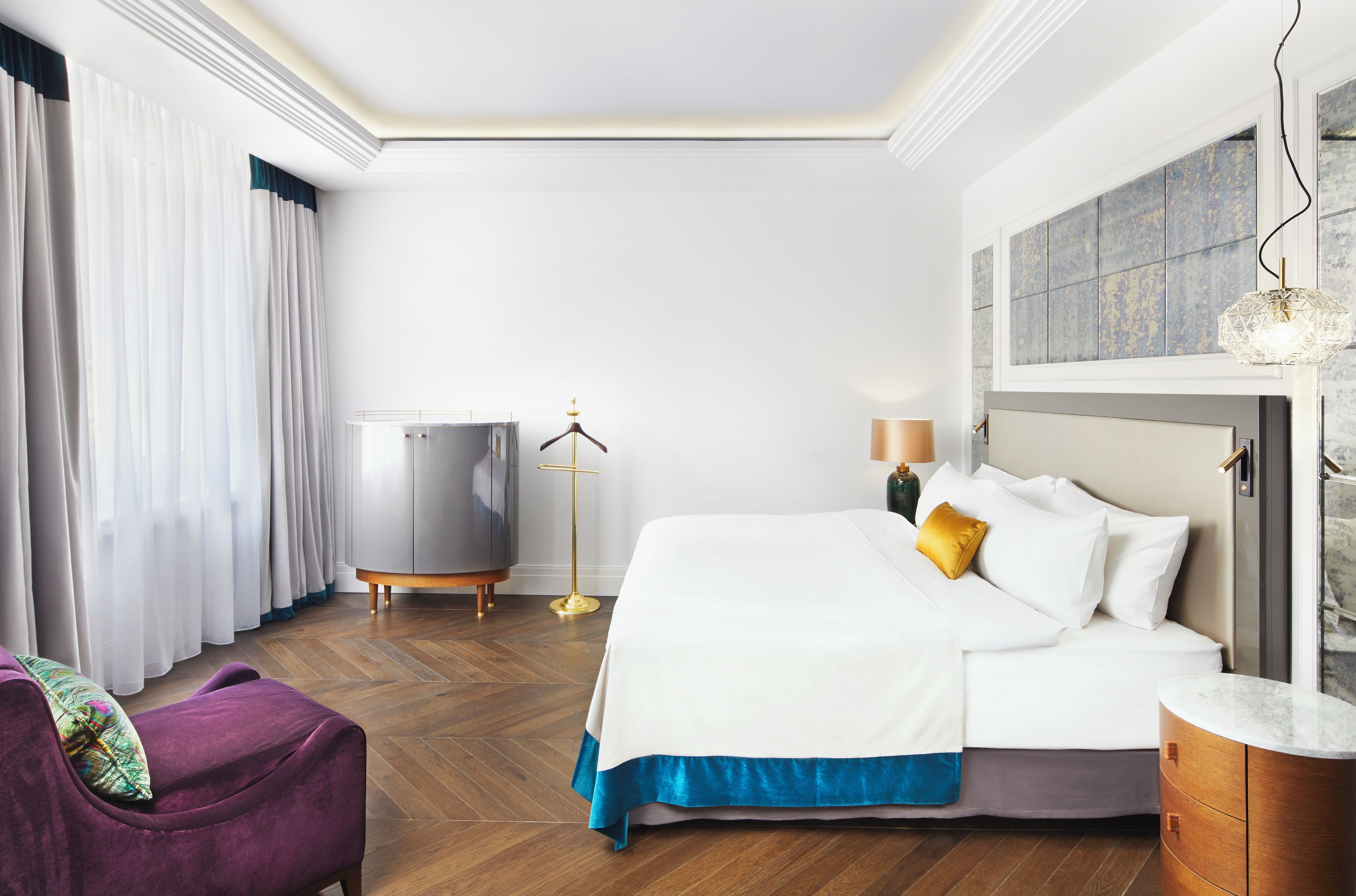 Habitación de hotel con cama, cómoda, silla, lámpara de pie y ventana con cortinas.