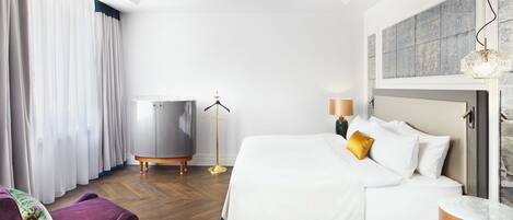 A hotel room with a bed, a dresser, a chair, a floor lamp, and a window with curtains.
