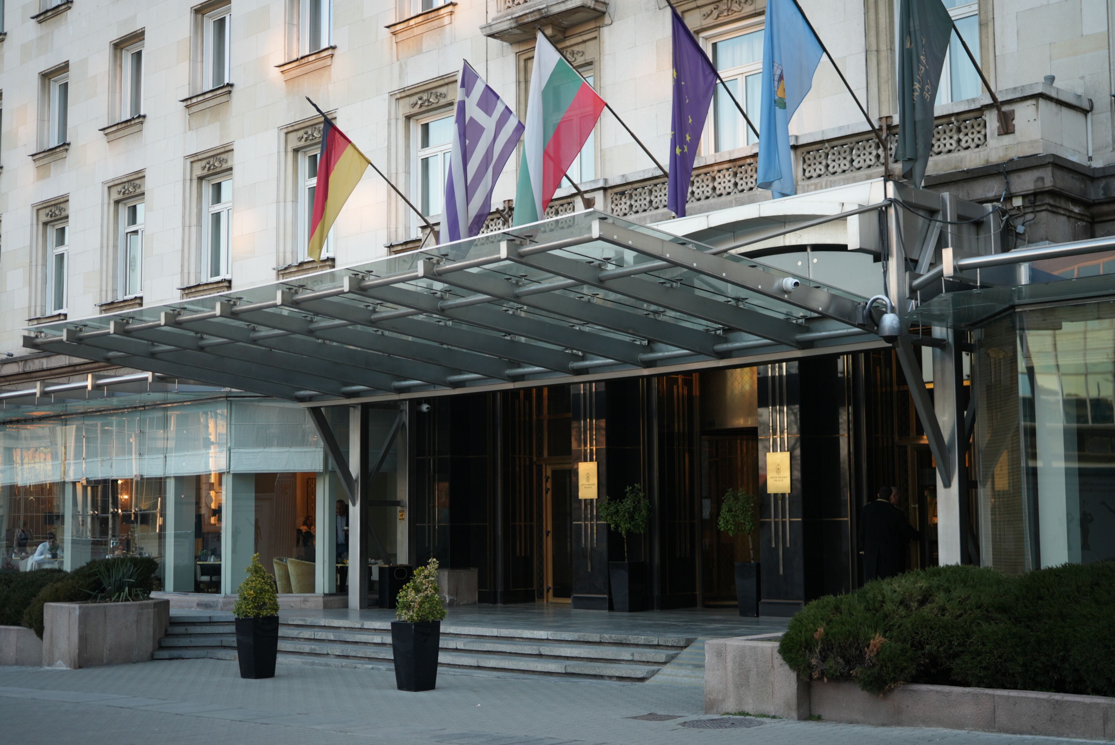 A hotel entrance with a glass facade, multiple flags, and a covered entrance area.