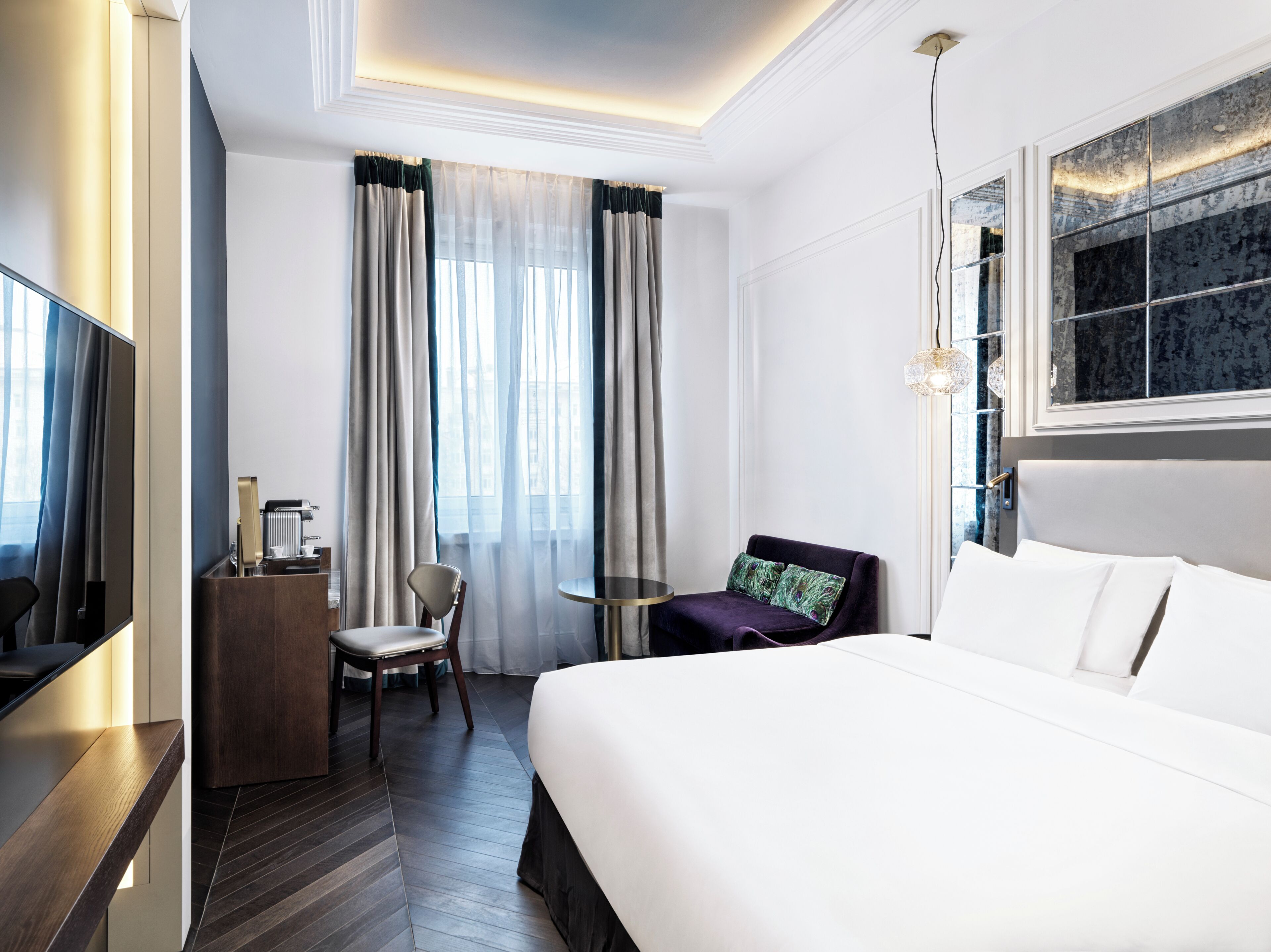 A hotel room with a bed, a desk, a chair, a small table, and a TV.