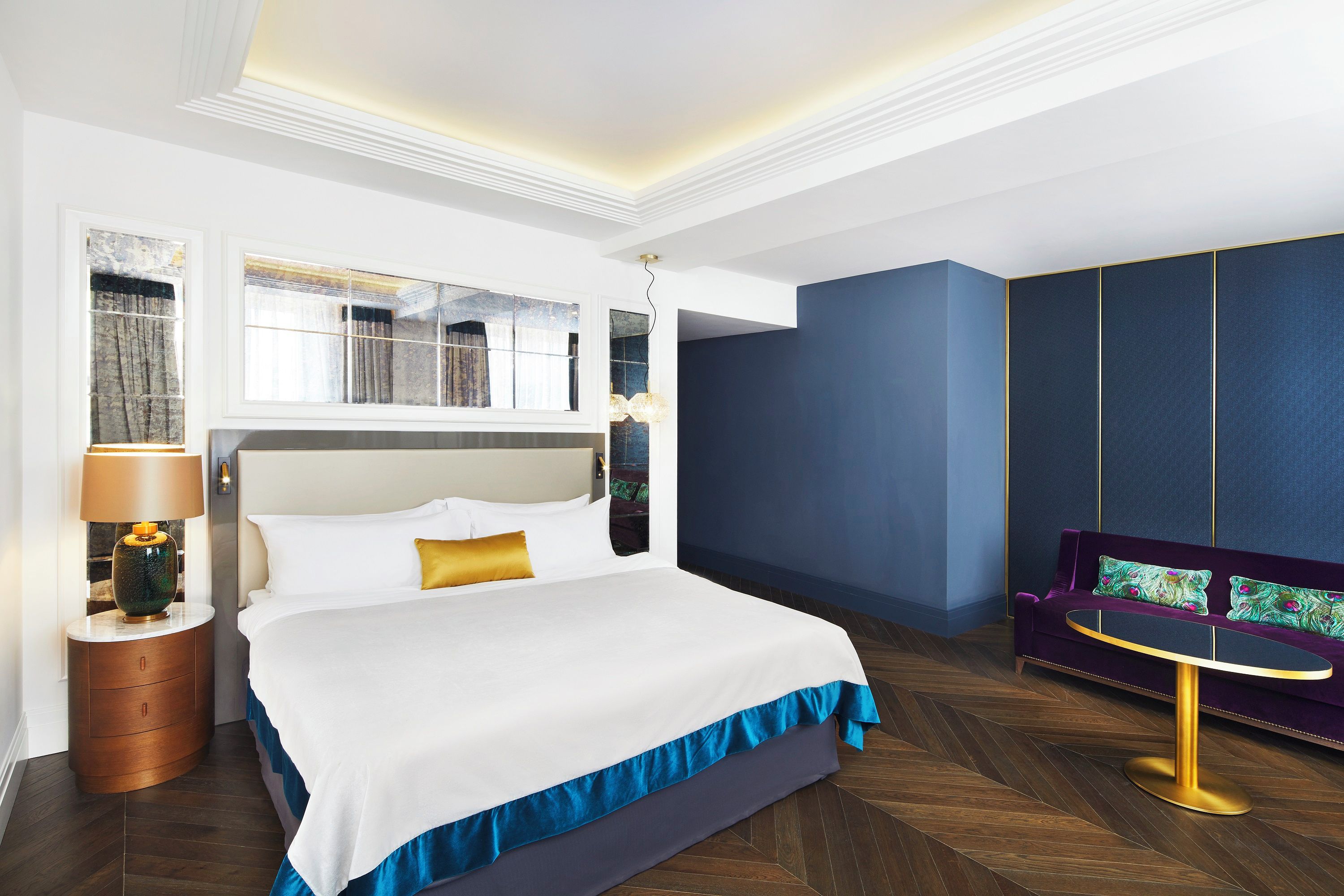 Une chambre d’hôtel avec un grand lit, une table de chevet, une lampe, un canapé et une vue sur l’extérieur.
