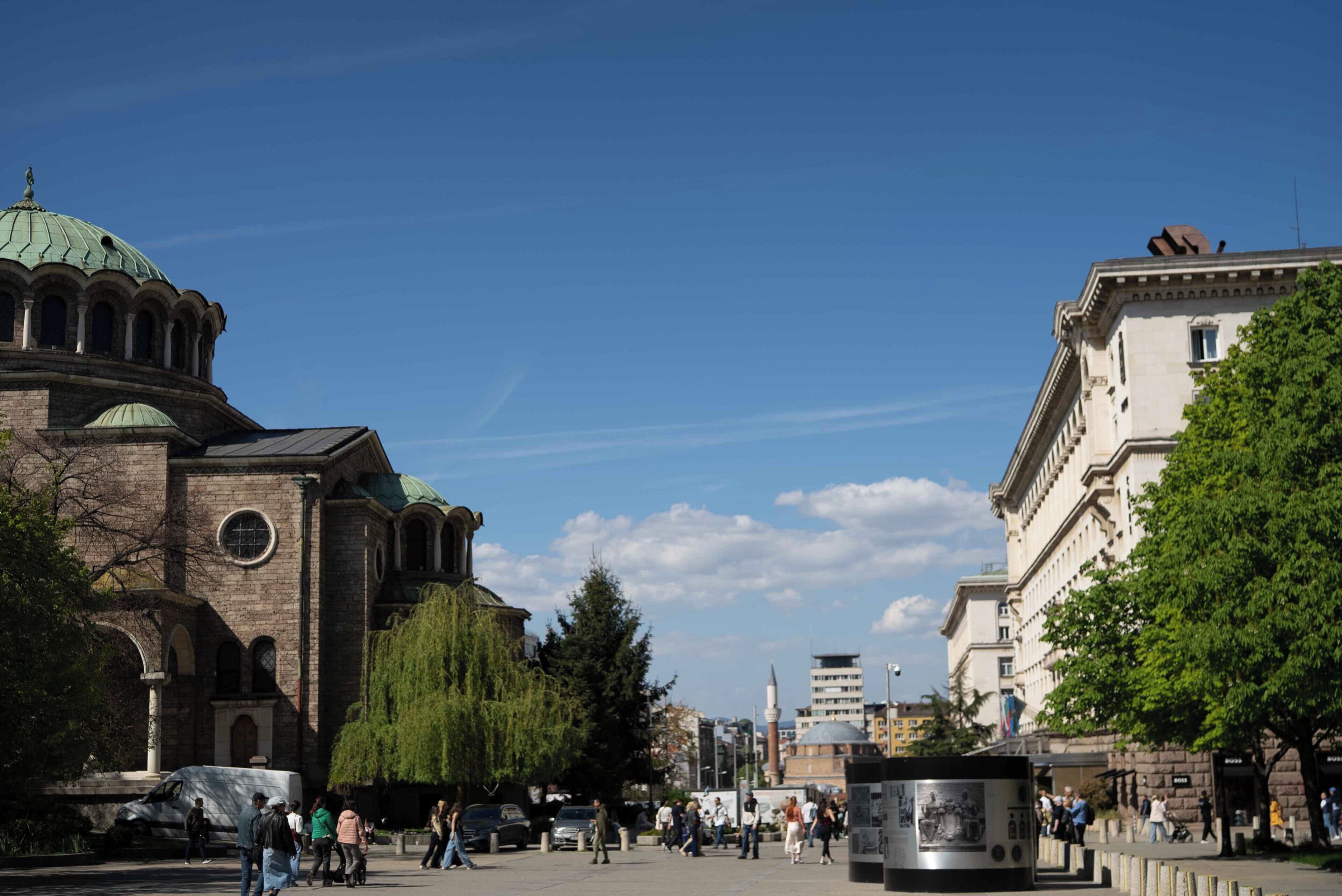 Ein historisches Gebäude mit einer Kuppel, einem großen Baum und einem modernen Bau im Hintergrund.