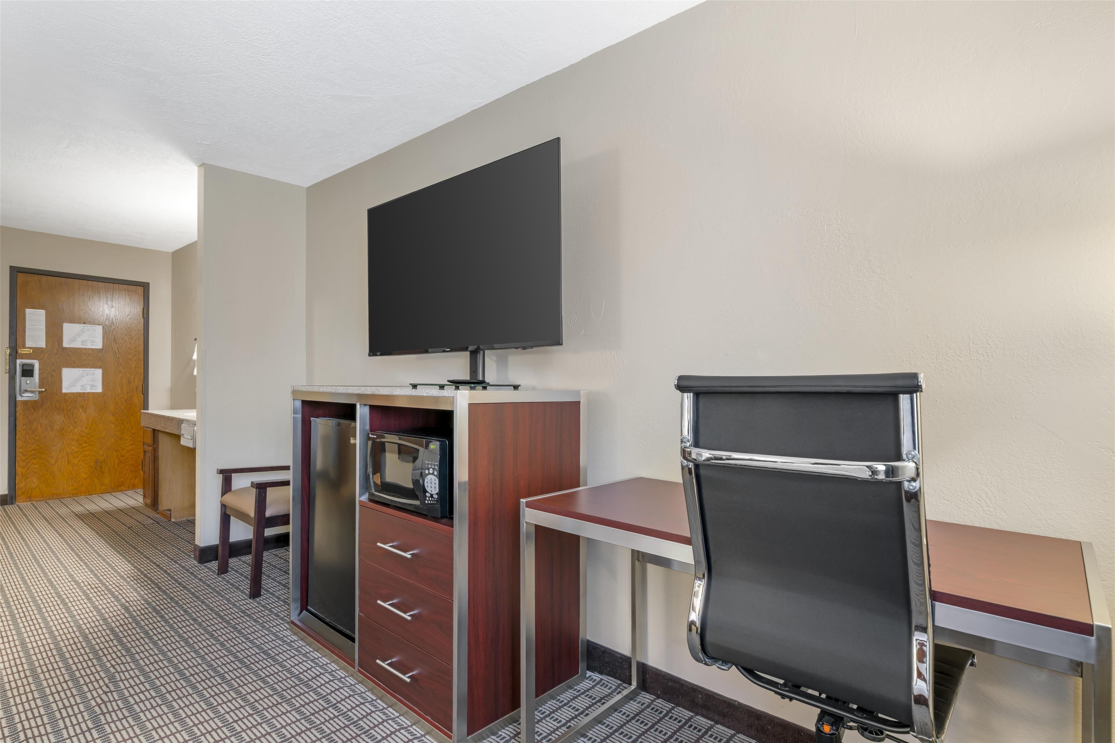 Une chambre d’hôtel équipée d’une kitchenette, d’un téléviseur à écran plat, d’un bureau avec une chaise et d’une porte avec un cadre en bois.