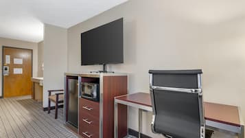 A hotel room with a kitchenette, a flat-screen TV, a desk with a chair, and a door with a wooden frame.