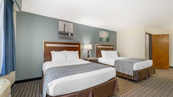 A hotel room with two beds, a nightstand with a lamp, a wall with a lighthouse picture, and a door.